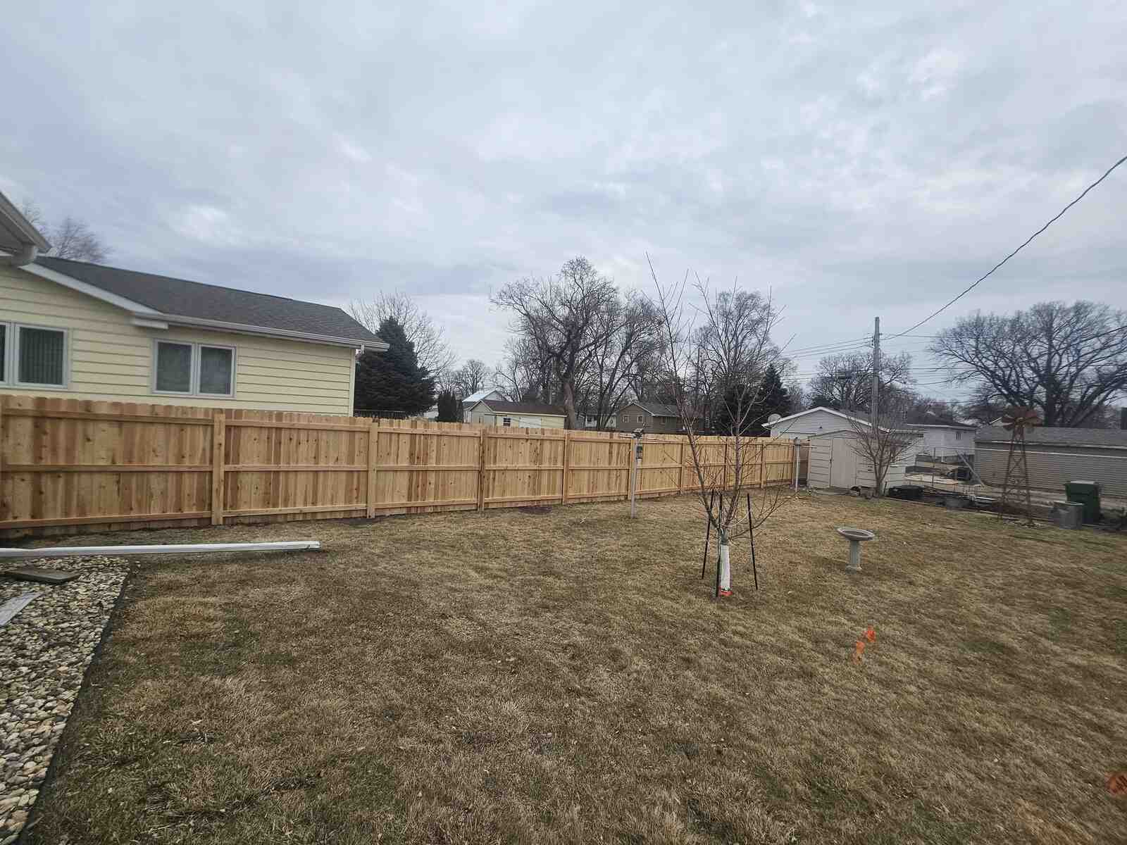 Cedar privacy fence with a birdbath and windmill ornament in the yard