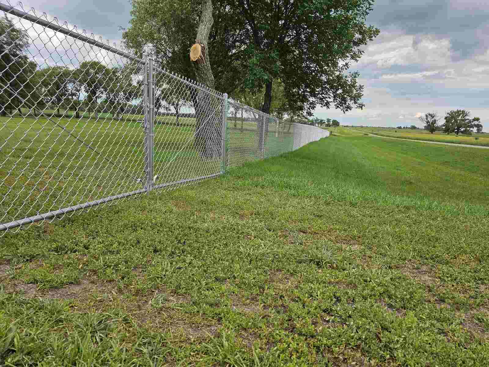 Galvanized chain link fence in an open field under a cloudy sky
