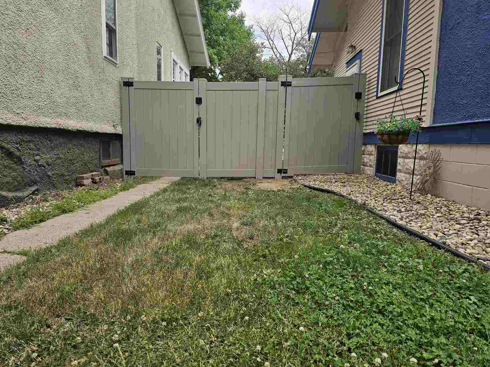 Gray vinyl privacy fence gate with stone landscaping