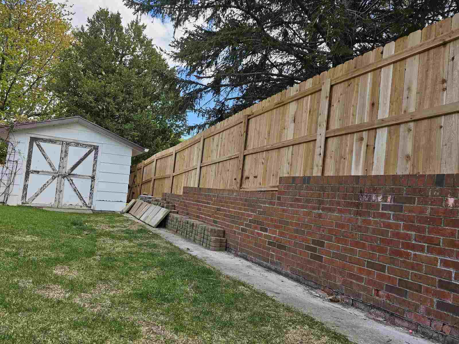 Tall cedar privacy fence above a brick retaining wall