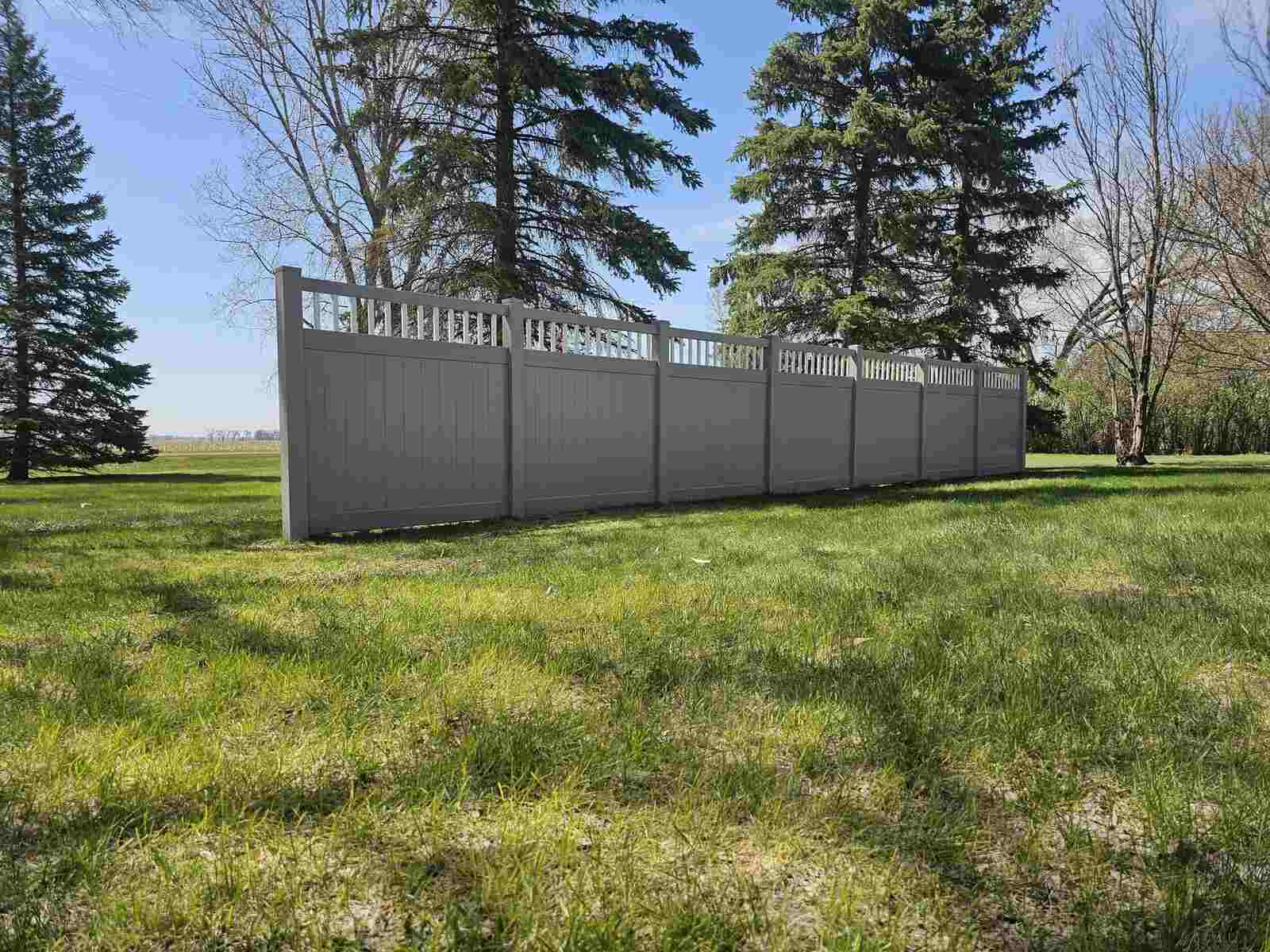 Gray vinyl privacy fence with a decorative picket top by evergreens