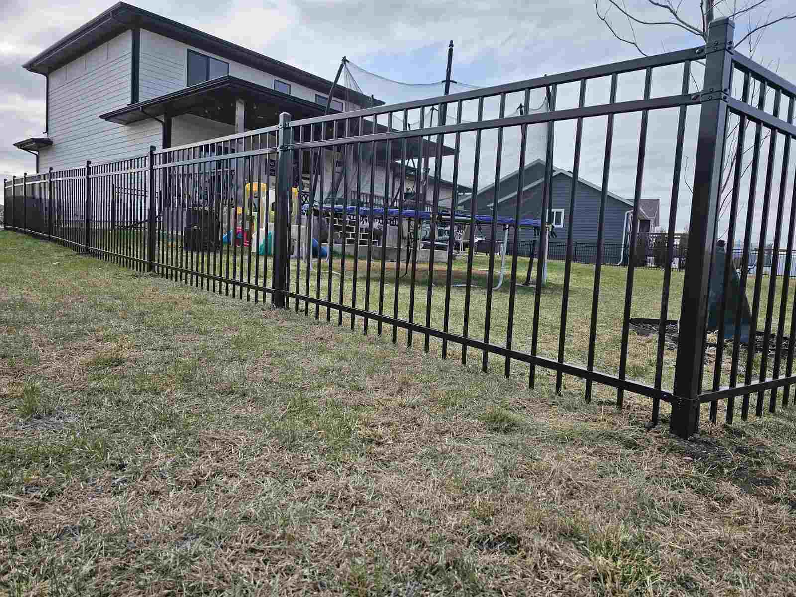 Black ornamental fence enclosing a property with a playground and trampoline